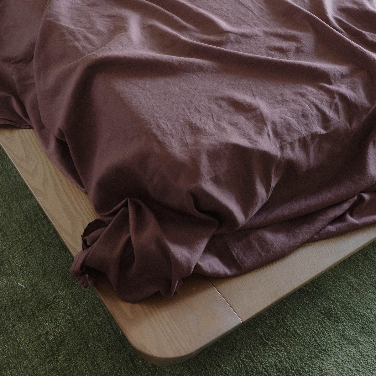 Close up on a corner of the bed, there are purple / brown sheets and the carpet is green