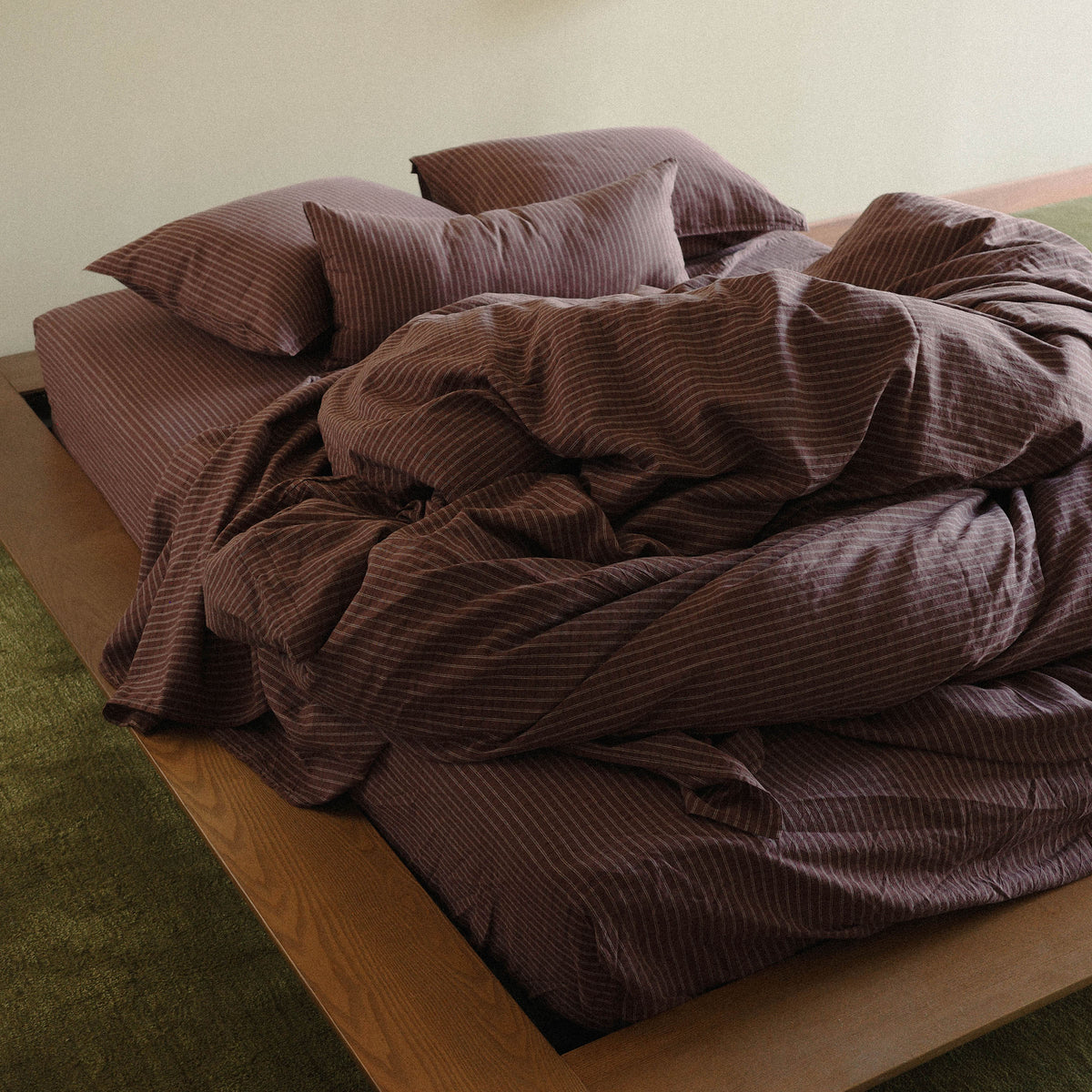 A brown Striped duvet cover and three pillows crumpled tastefully on a wooden bed.