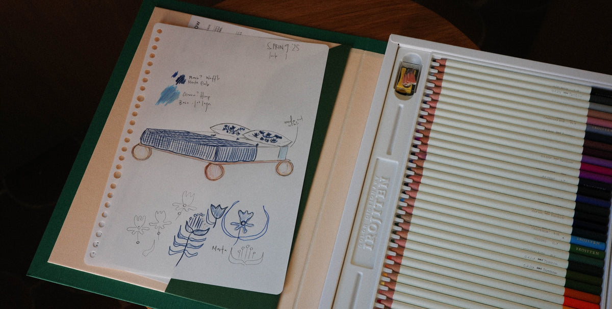 A colored pencil set shown open, revealing a lined white pencil box with colored pencils on the right and a lined sketchbook on the left.