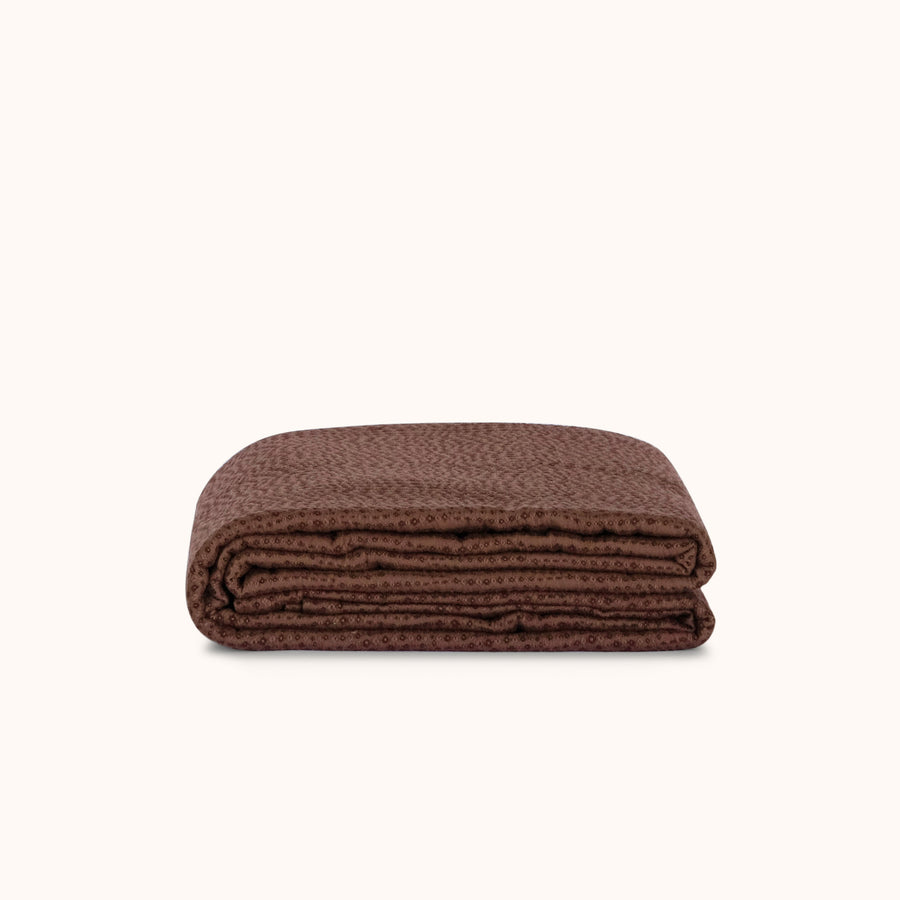 Folded brown coverlet on a white background