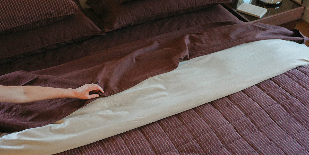 Person adjusting a flat sheet on a bed with brown bedding.