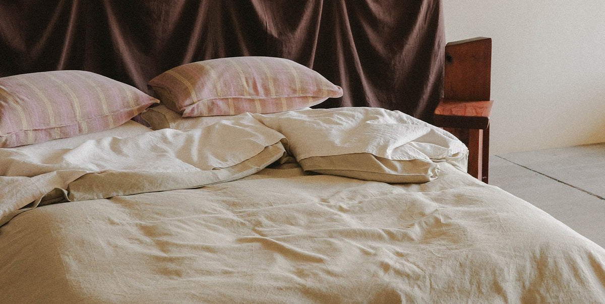 Bed with light green and cream bedding and pink striped pillows against a dark brown headboard.