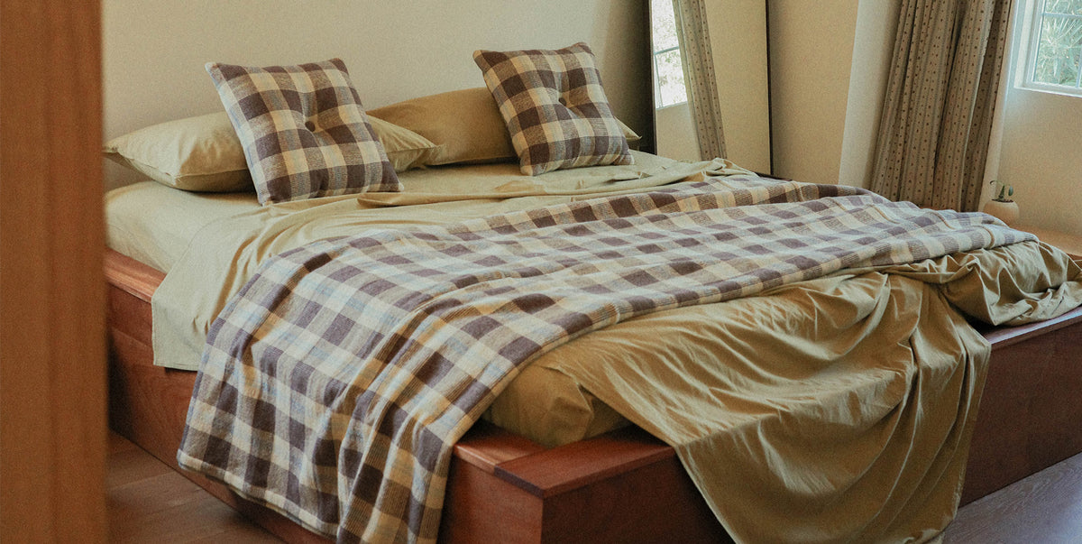 Bed with plaid blanket and pillows in a room with curtains and a window.