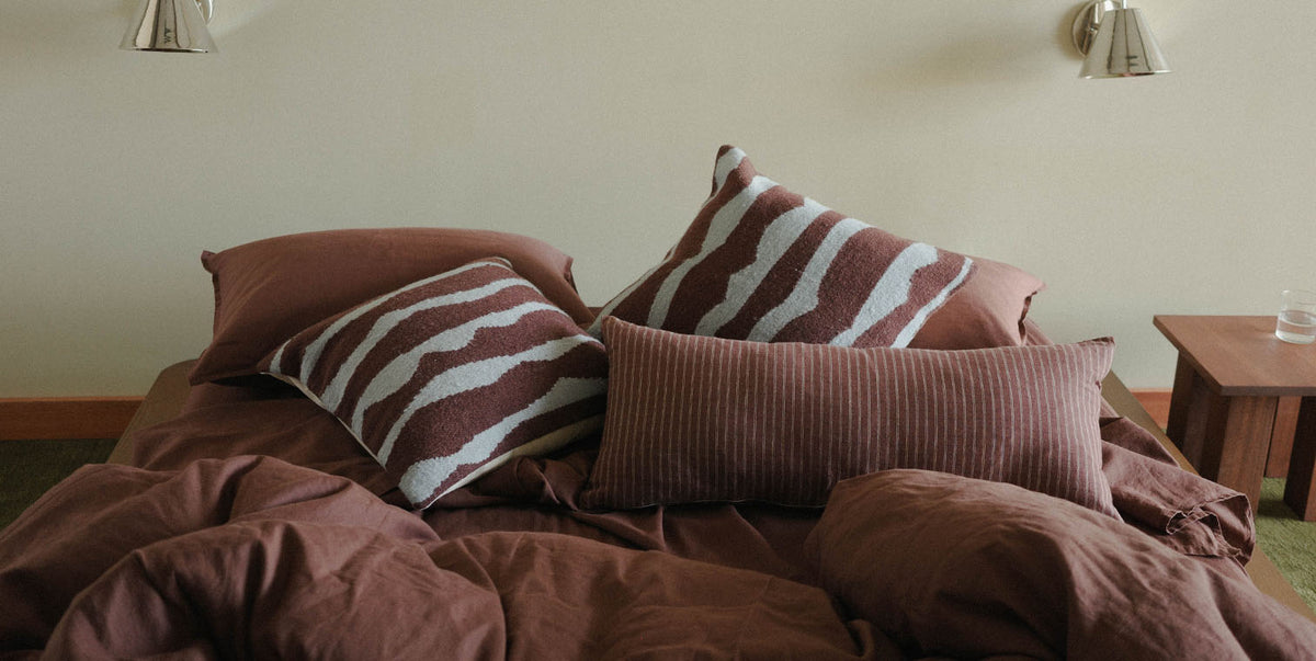 Bed with brown bedding and striped pillows in a room setting.