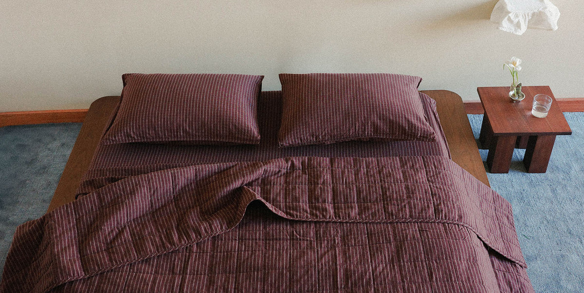 Brown plaid bedspread and pillows on a bed in a room with a wooden table and vase.