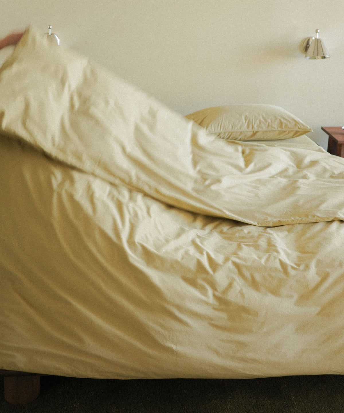 Person fluffing a green duvet on a bed