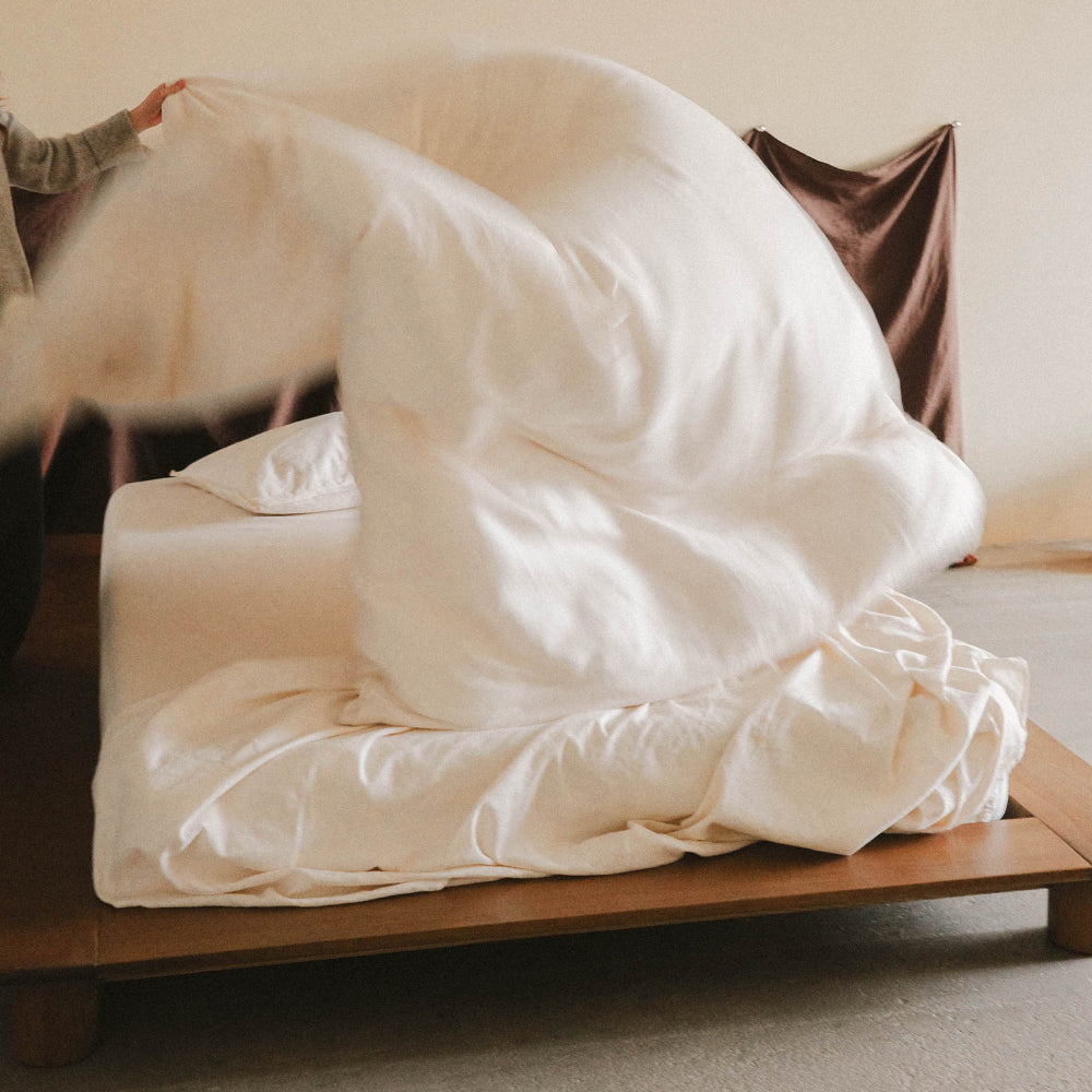 Person fluffing a white duvet on a bed