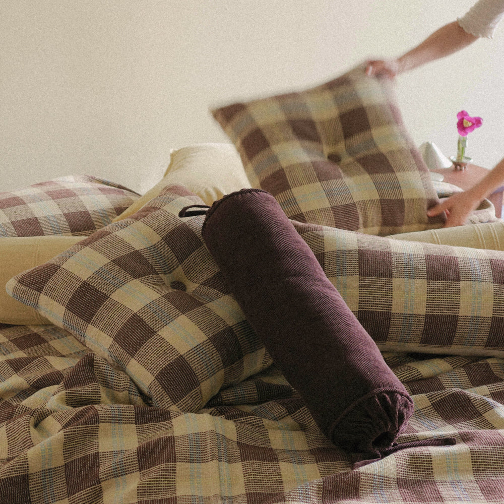Person grabbing a stack of brown and yellow checked pillows