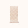 A rectangular, blush-colored bath mat with a subtle check pattern and contrasting shag heights.